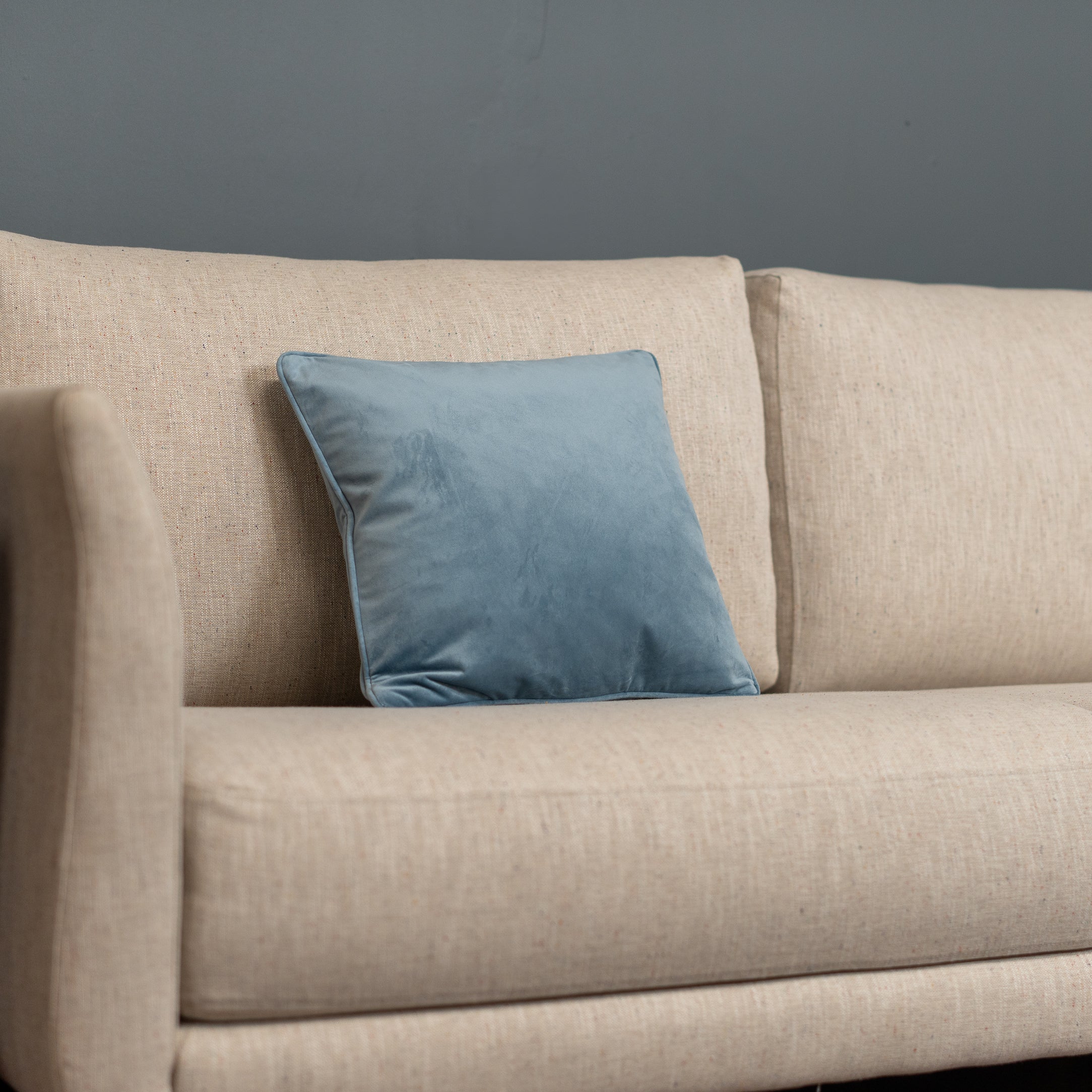 Beige sofa with a blue pillow against a gray wall