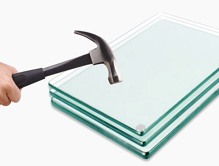 Hand holds hammer over stacked glass panels, poised to strike.