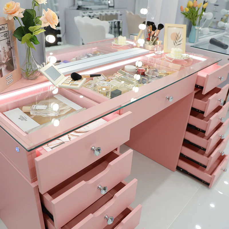 a pink vanity table with an illuminated mirror, multiple drawers