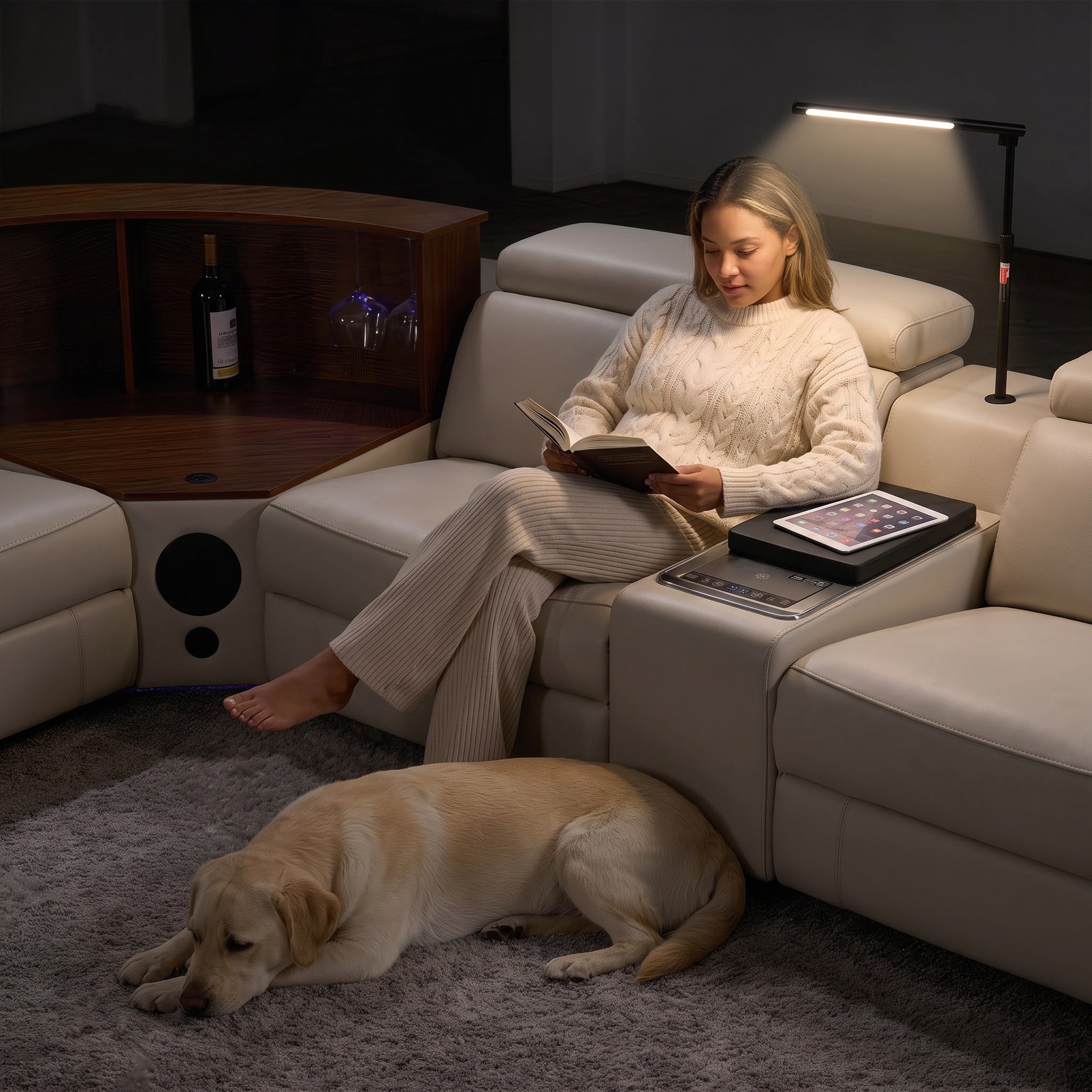 A woman is reading a book while using the lighting fixture on the sofa.